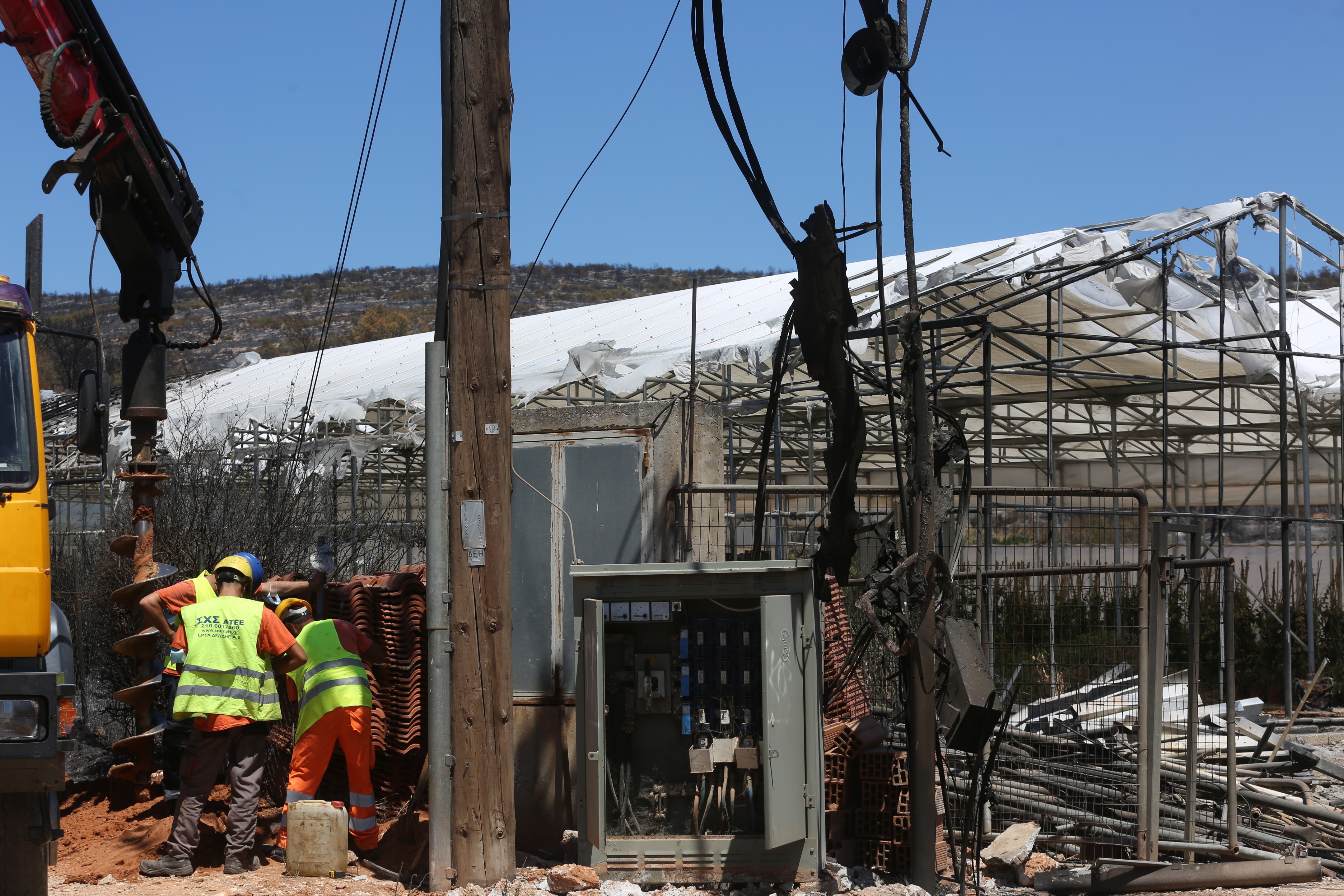 Workers try to fix a burnt power pillar in front of a burnt greenhouse after a wildfire in the area of Marathon, Attica region, Greece, 13 August 2024. A wildfire that broke out on 11 August in the outskirts of Athens and spread to a large part of northeastern Attica no longer had a single front on 13 August. The fire stretched along a front more than 30 kilometres in length. According to the Fire Brigade, the firefighting forces are dealing with scattered pockets of fire from Varnavas to Nea Makri and Penteli while there are constant rekindlings. Firefighters found a charred body, of a 60-year-old woman, in a small factory that caught fire in Patima Halandriou.  EPA/ALEXANDROS BELTES