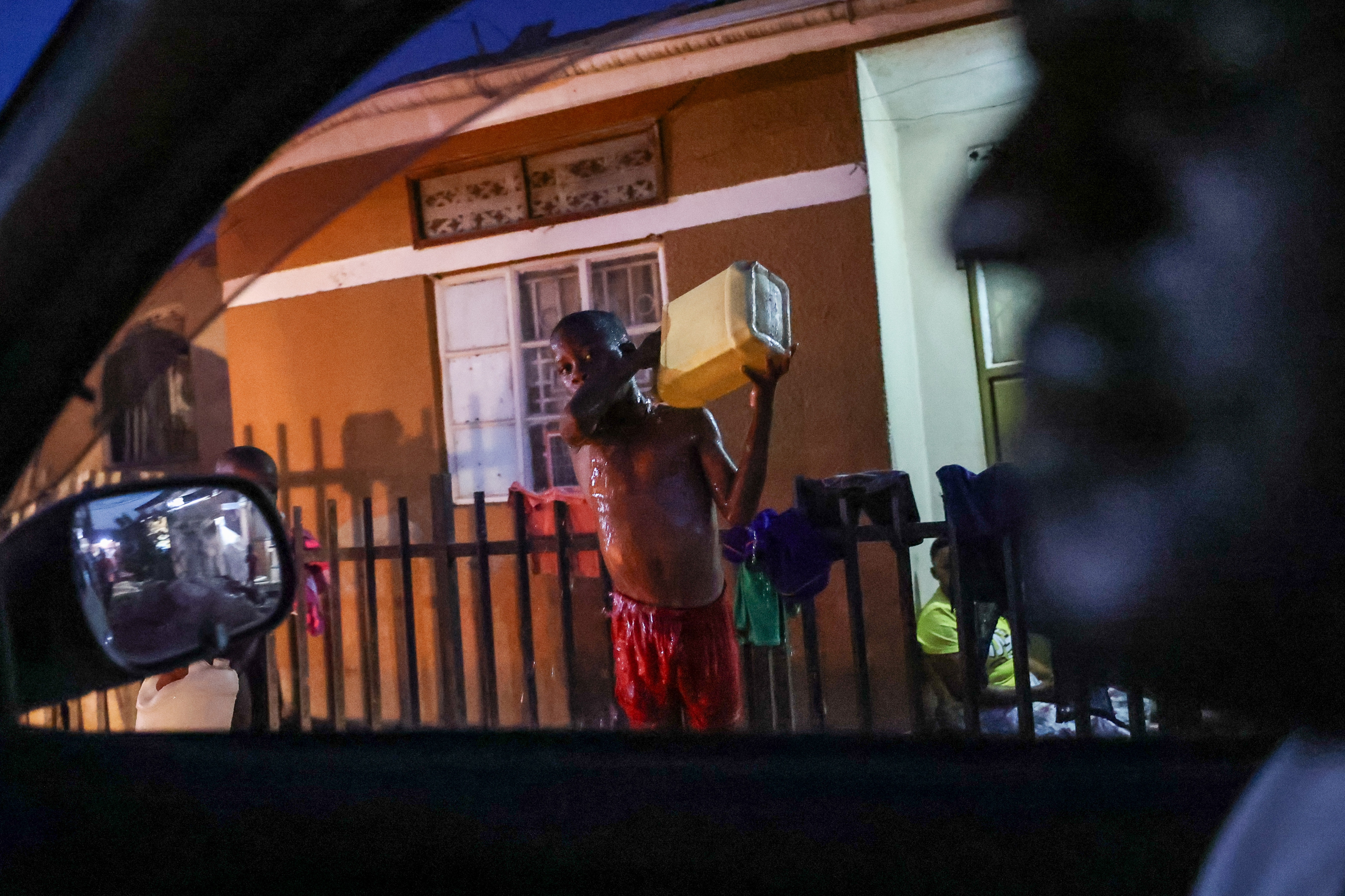 A young person (C) takes a bath using a jerrycan outside their house in the Kitintale slum area of Kampala, Uganda, 19 January 2026. The Ugandan Electoral Commission declared incumbent Yoweri Museveni president-elect after elections held on 15 January 2026. EPA/DANIEL IRUNGU