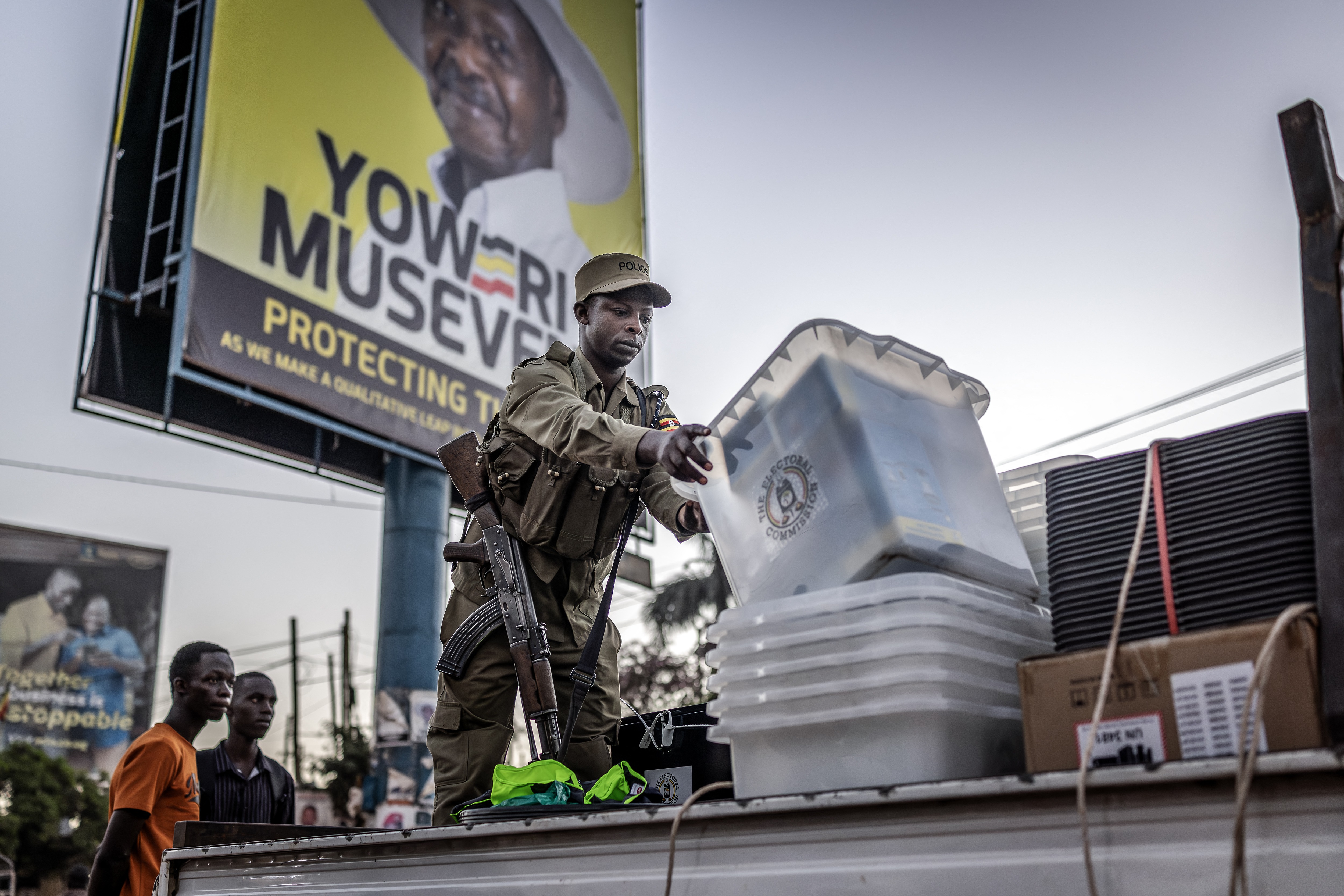 A Ugandan police officer unloads ballot boxes from a truck at a polling station set up in front of an electoral billboard supporting Uganda's incumbent president and National Resistance Movement (NRM) presidential candidate, Yoweri Museveni, in Kampala on 15 January 2026, during Uganda's 2026 general elections. (Photo: Luis TATO / AFP)