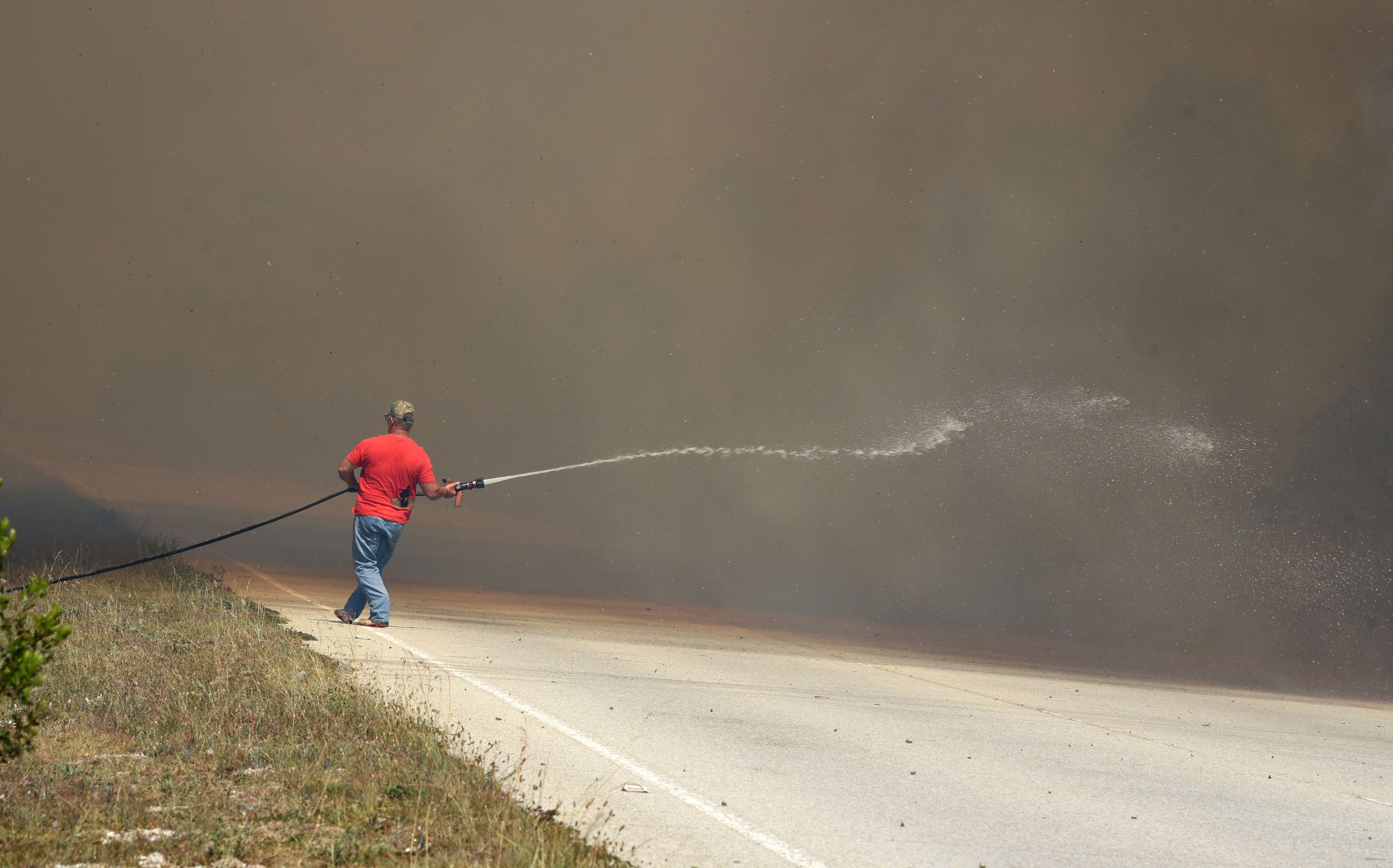 Dense smoke from a veld fire along the N2 reduces visibility as a man drags a firehose in an effort to contain the blaze. (Photo: Deon Ferreira)