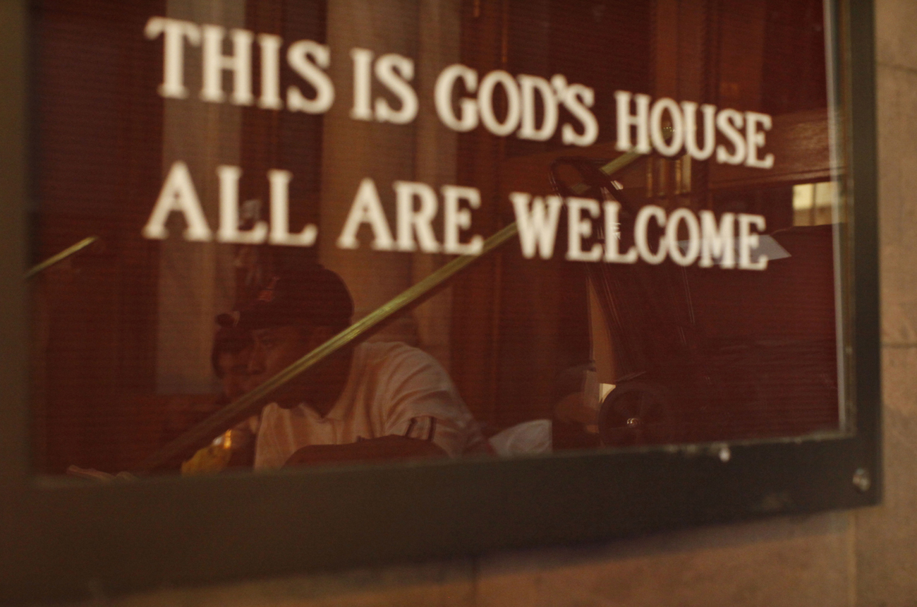 Homeless people are reflected in a window at the entrance of a church in New York