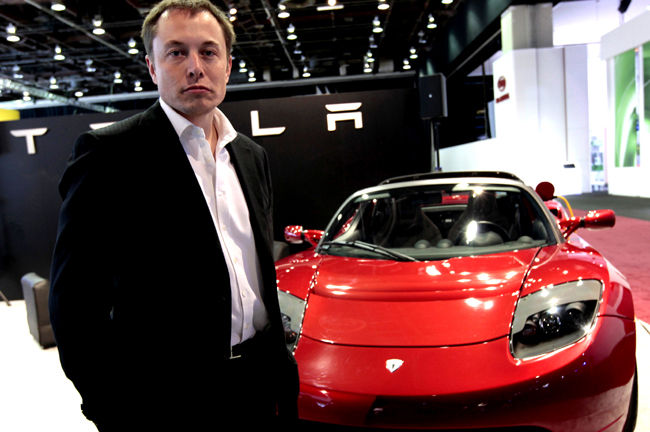 Tesla Motors Inc. CEO and Chairman Elon Musk stands in front of the Tesla Roadster electric vehicle as he addresses the media during press days of the North American International Auto Show in Detroit,