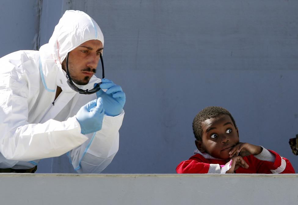A rescue worker gestures next to a child as they arrive on the Italian naval vessel Fugida, in the Sicilian harbour of Augusta
