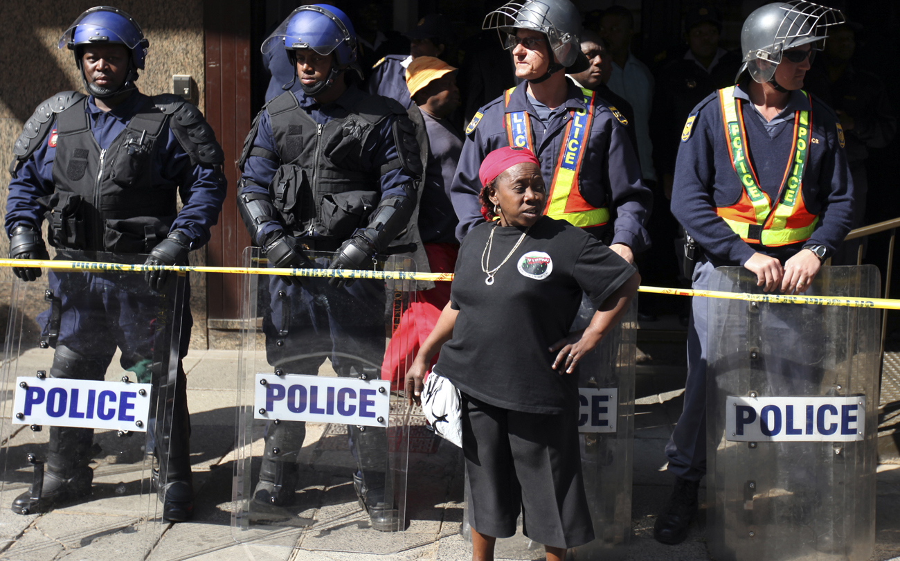 Police keep watch as a South African state worker seeking higher wages looks on during in a strike in Johannesburg