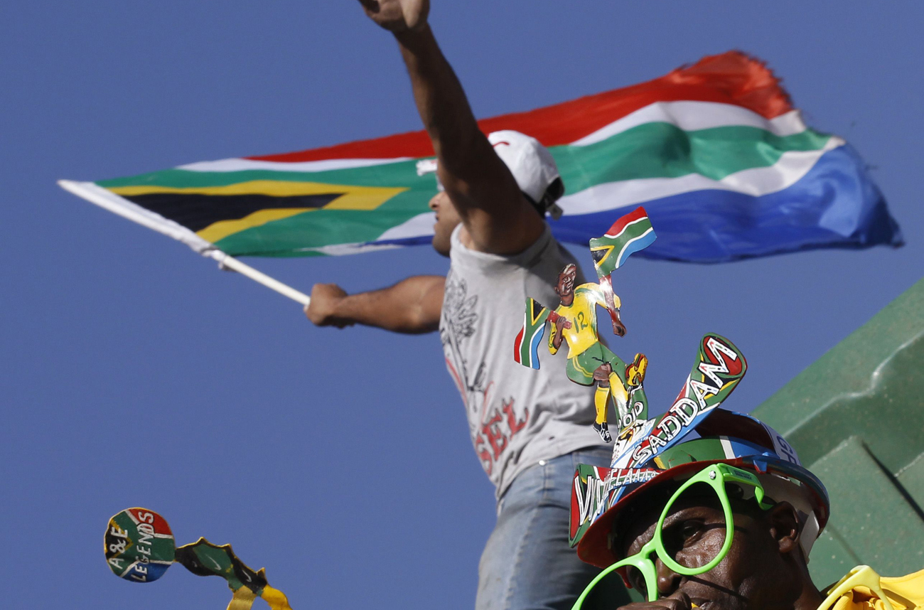 A South African soccer fan blows a vuvuzela while another waves the national flag as they wait for their national soccer team "Bafana Bafana" during a parade on the streets of Sandton in Johannesburg