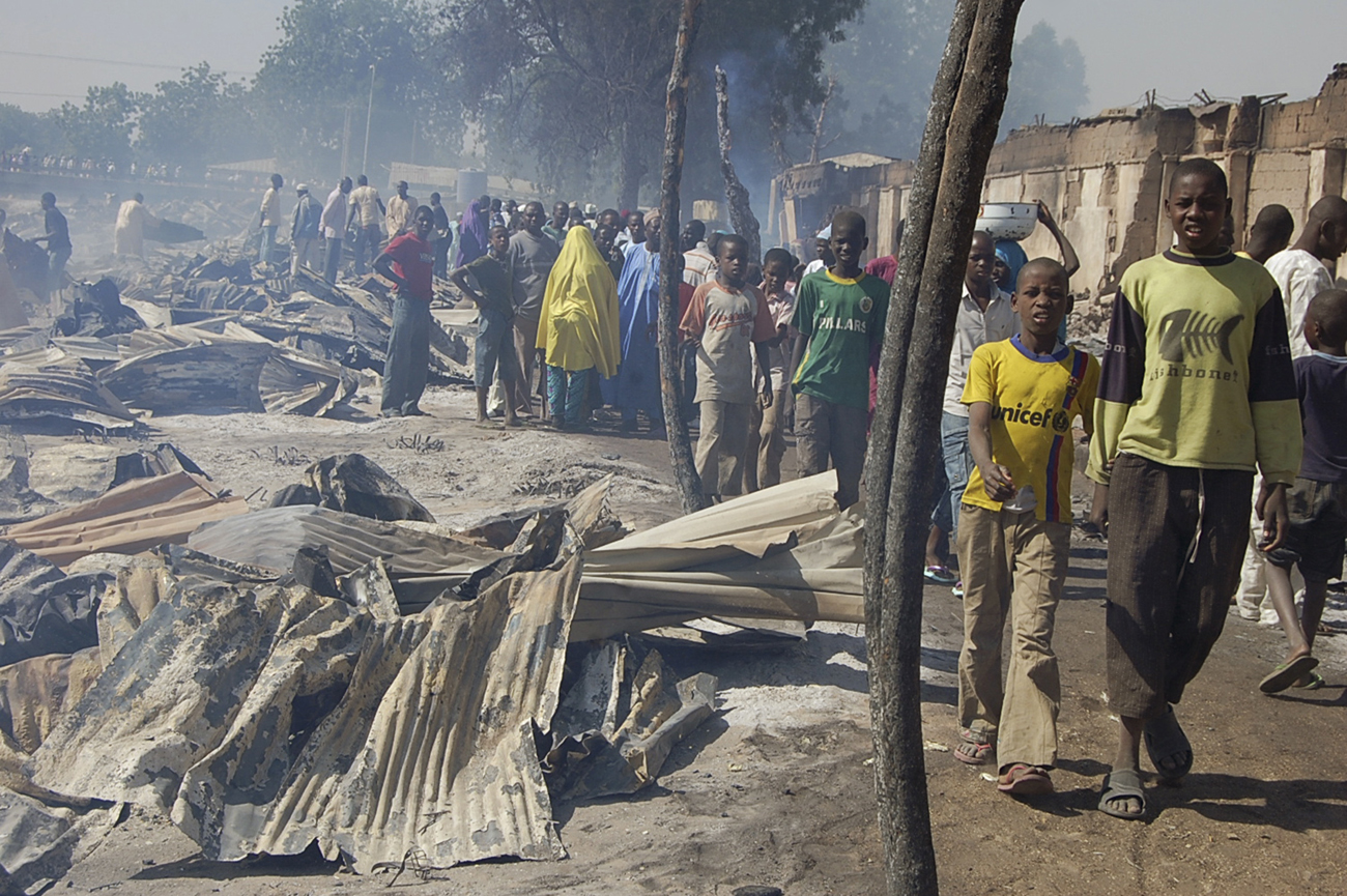 People walk past burnt roofing sheets after a fire razed Gombomru main market in Nigeria's northeastern city of Maiduguri