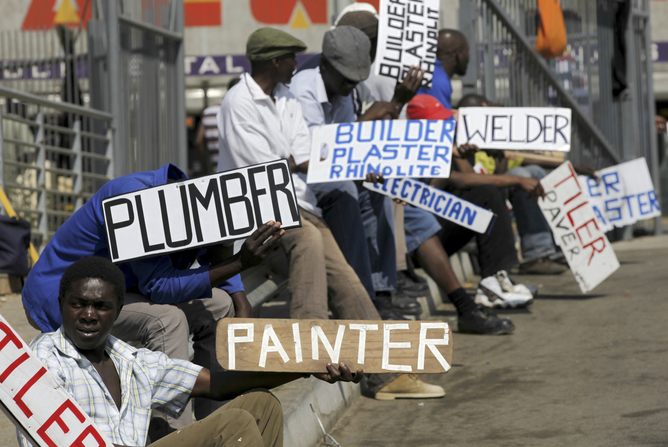 Men hold placards offering temporal employment services in Glenvista, south of Johannesburg