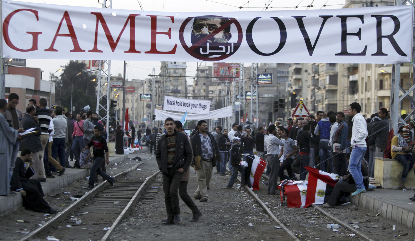 Anti-Mursi protesters walk near banner in front of the presidential palace in Cairo