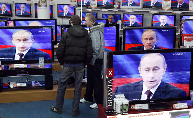 Men look at a television screening of Russia?s PM Putin speaking in Moscow