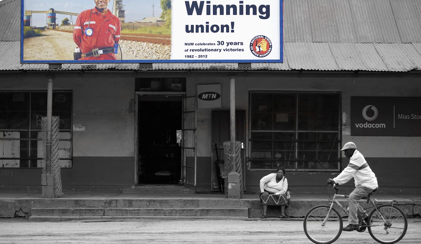 A woman sits beneath a recruitment poster for the National Union of Mineworkers near Rustenburg in the North West province
