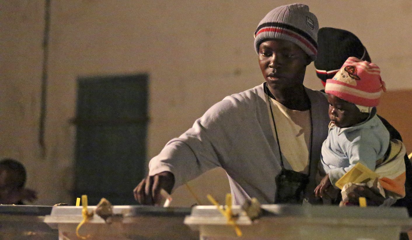 Woman carrying a child casts her vote at a polling station in Domboshava
