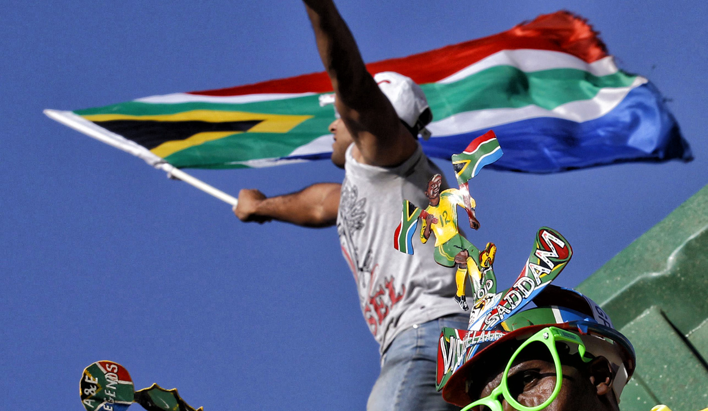 A South African soccer fan blows a vuvuzela while another waves the national flag as they wait for their national soccer team "Bafana Bafana" during a parade on the streets of Sandton in Johannesburg