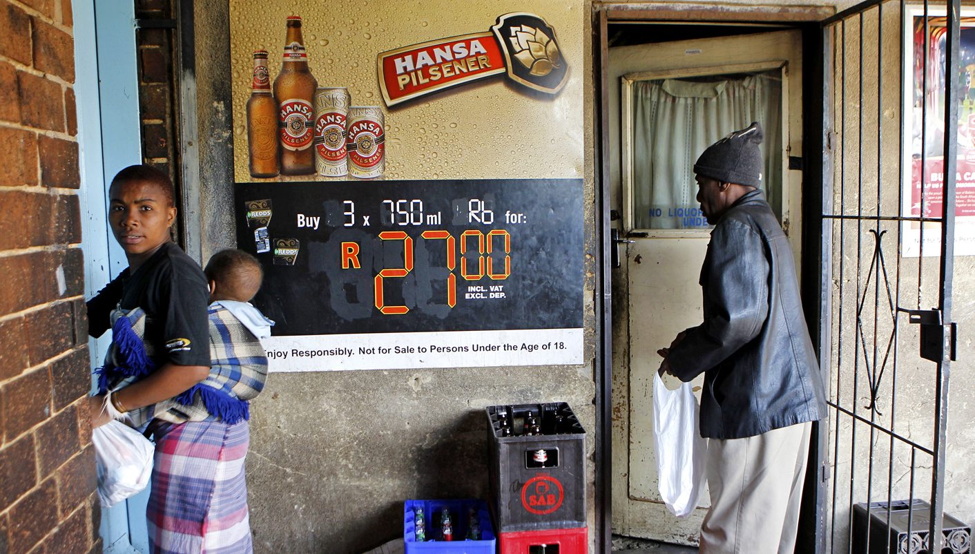 A man waits for his beer as a woman carrying a baby walks past at a sheeben in Soweto, southwest of Johannesburg