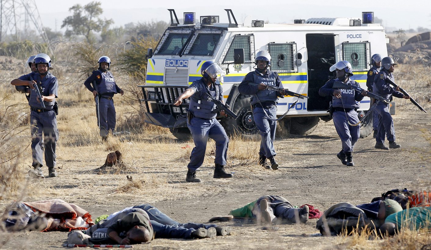 A policeman gestures in front of some of the dead miners after they were shot outside a South African mine in Rustenburg