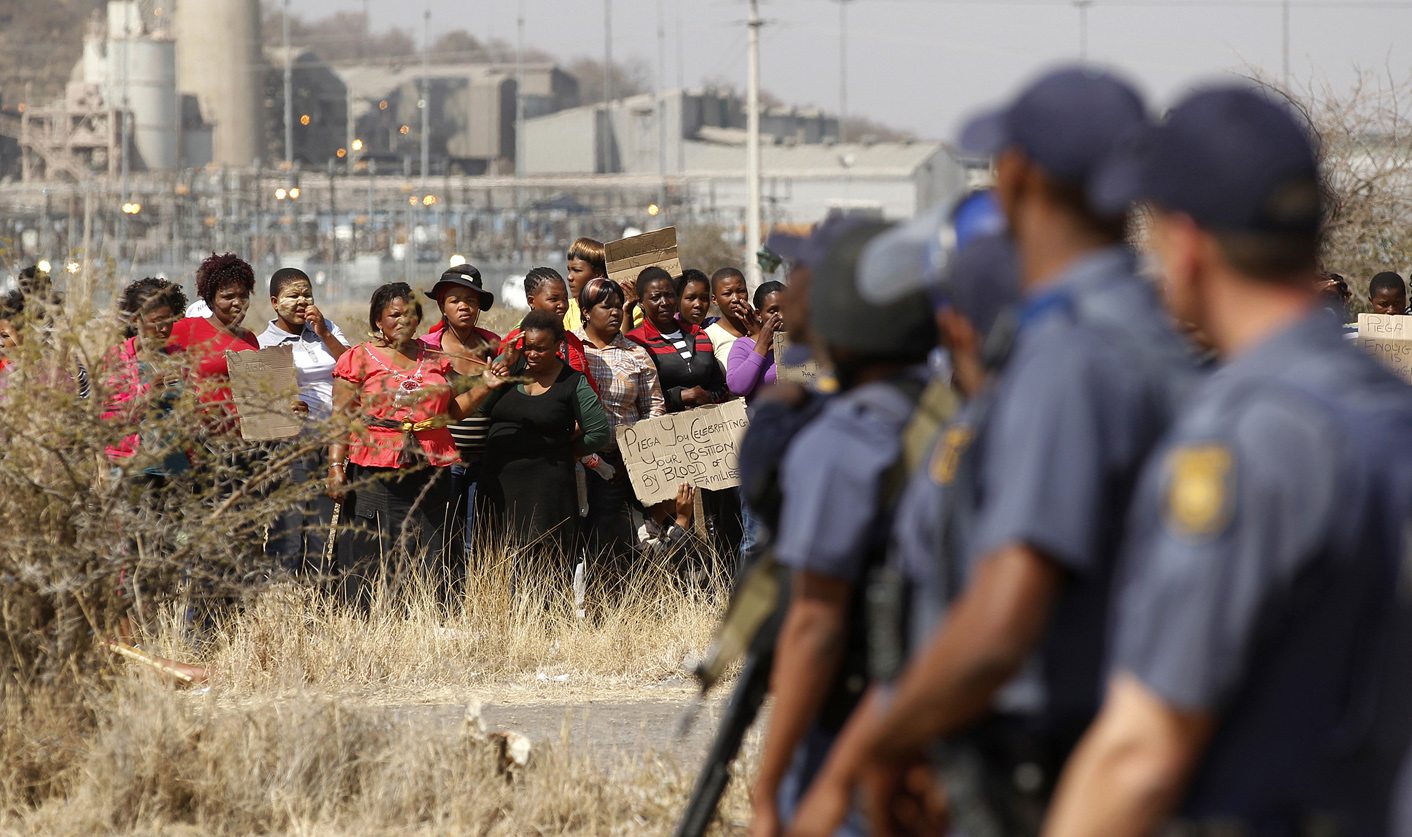 Police look on as women carry placards in protest against the killing of miners by the South African police on Thursday, outside a South African mine in Rustenburg