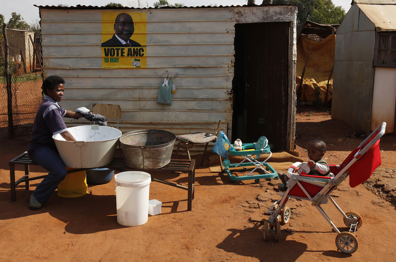 Mother washes clothes as ANC election poster is seen on shack she and her family live in at Waterworks, informal settlement outside Soweto