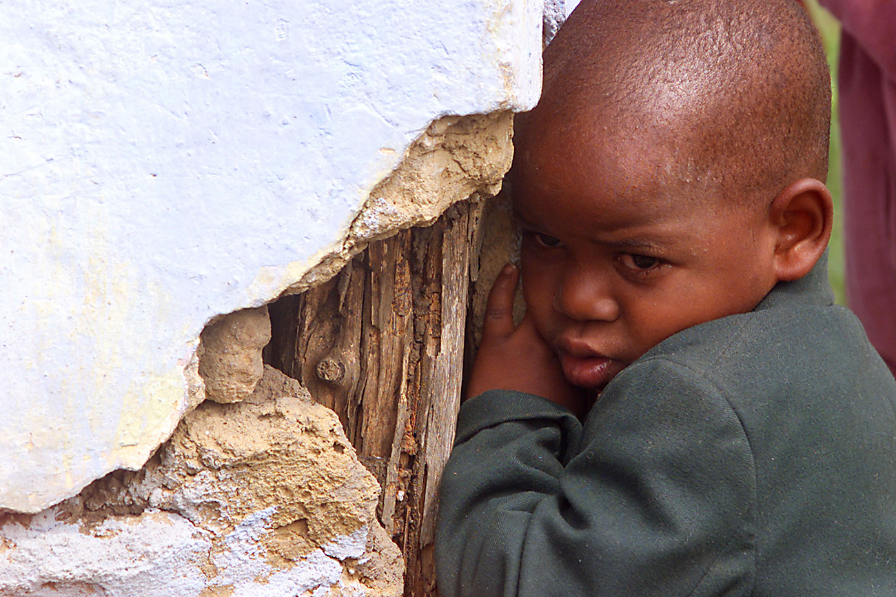 A YOUNG CHILD ORPHANED BY AIDS IN CLINGS TO A BROKEN CORNER OF HER HOME IN RURAL KWAZULU NATAL.