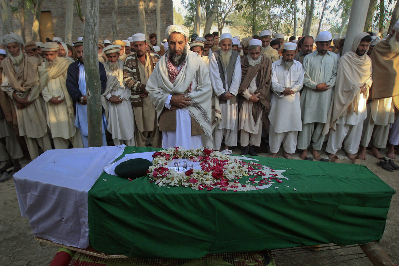 Relatives and residents pray near the flag-draped coffin of solider Najeebullah in his hometown Charsadda