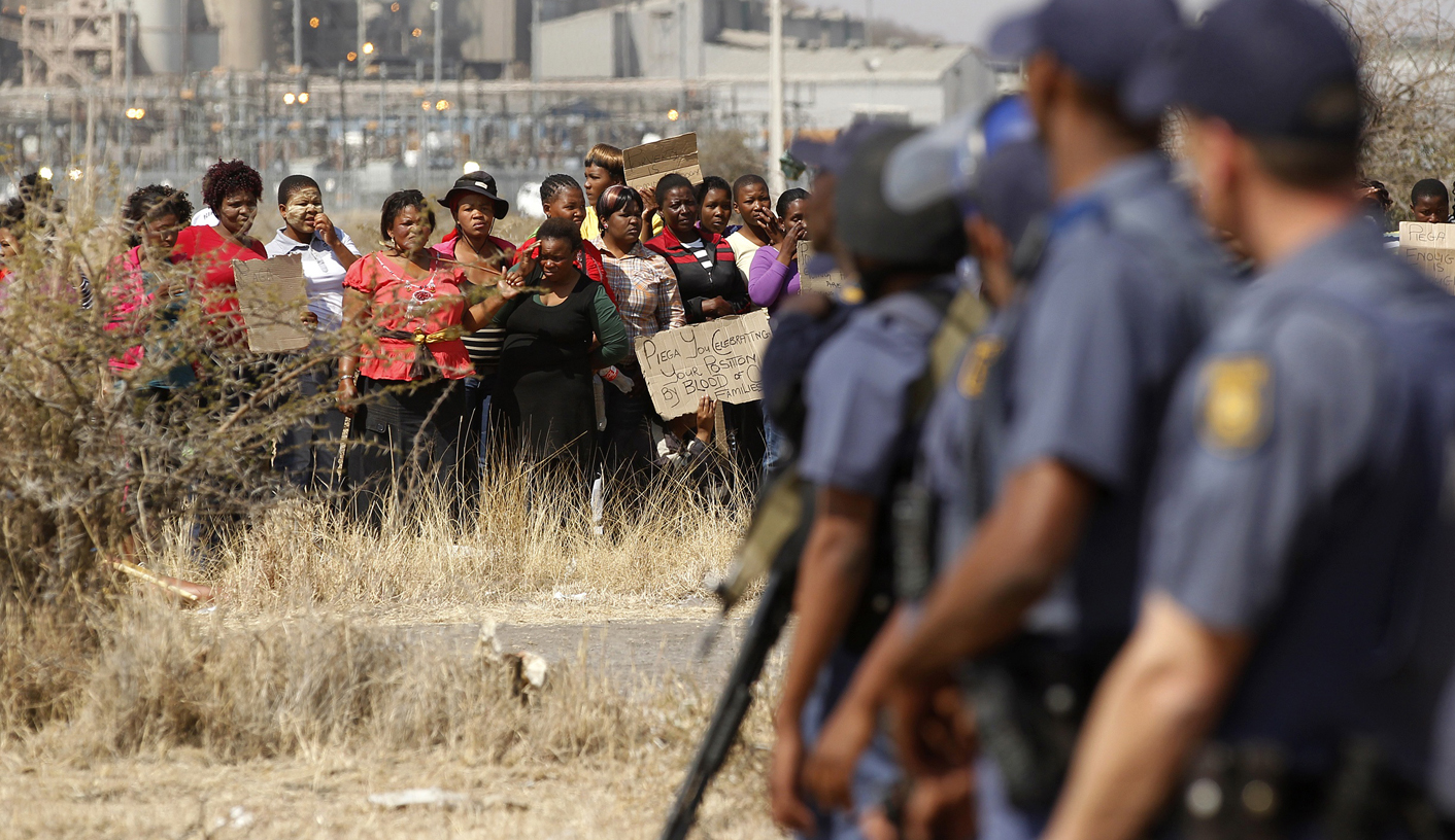Police look on as women carry placards in protest against the killing of miners by the South African police on Thursday, outside a South African mine in Rustenburg
