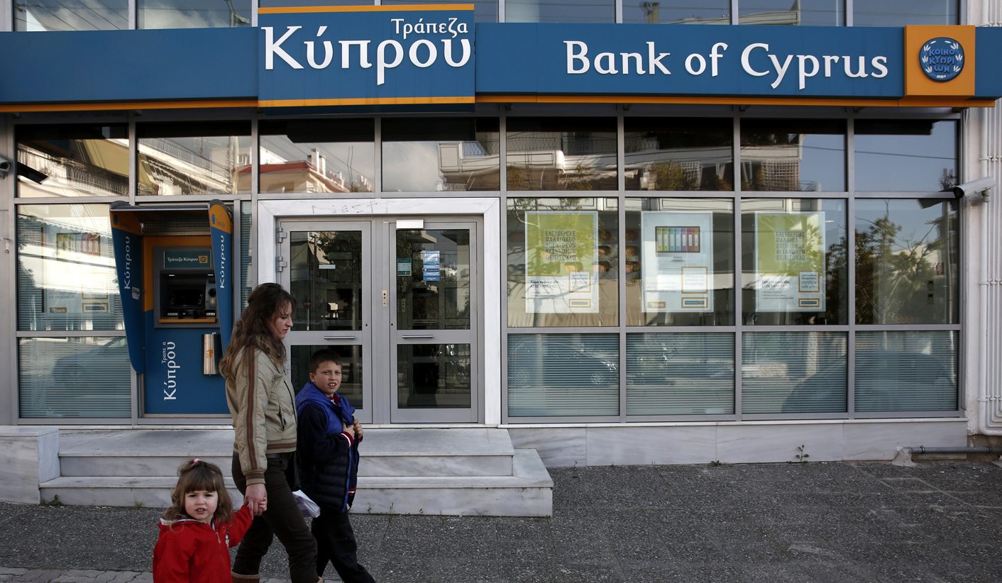A woman with children walks past a branch of Bank of Cyprus at Glyfada suburb in Athens