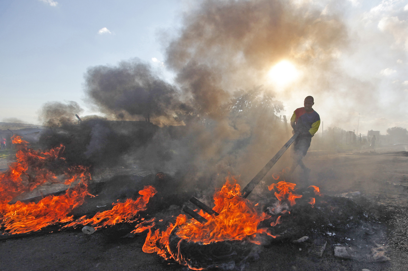 A township resident burns tyres and other materials to erect a barricade during protests over the delivery of basic housing and education near Ermelo