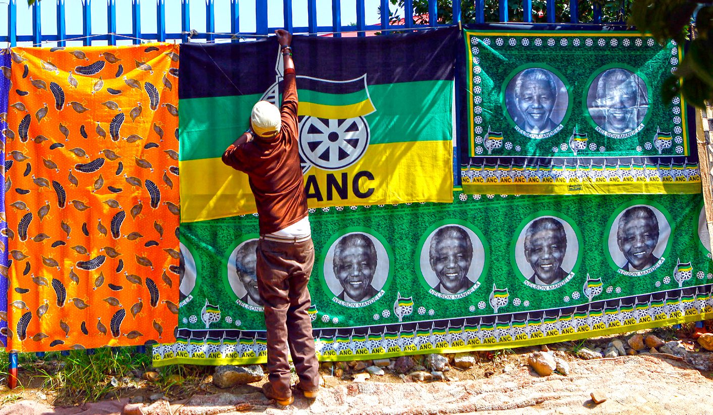 A man adjusts the ANC flag next to banners with images of former South African President Nelson Mandela and the colours of the ANC flag at a stall in Soweto
