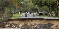 Residents walk near a section of a road that was washed away at the end of Holloways Beach Esplanade in Cairns, Queensland, Australia, 18 December 2023. Residents in far north Queensland are bracing for more rain and further significant flooding.  EPA-EFE/JOSHUA PRIETO AUSTRALIA AND NEW ZEALAND OUT