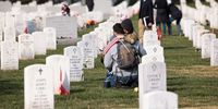 ARLINGTON, VIRGINIA - NOVEMBER 11: Army veteran Stephen Hedger is hugged by his son Lincoln as he visits the gravesite of U.S. Army Major Paul Douglas Carron at Arlington National Cemetery on Veterans Day, November 11, 2021 in Arlington, Virginia. During Veteran's Day, military members, veterans and their loved ones visited the cemetery to pay their respects to those they have lost. (Photo by Anna Moneymaker/Getty Images)