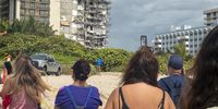 Few persons observe the partially collapsed 12-story condominium building in Surfside, Florida, USA, 25 June 2021. Miami-Dade Mayor Daniella Levine Cava said on 25 June morning that the number of people who are unaccounted for in building collapse in Surfside rose to 159, while the death toll rose to four.  EPA-EFE/CRISTOBAL HERRERA-ULASHKEVICH