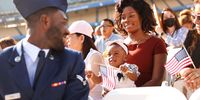 LOS ANGELES, CALIFORNIA - AUGUST 29: U.S. Air Force Airman Michael Drah (L), originally from Ghana, smiles with his wife Akosua Yeboah-Drah and daughter Rashana Drah before he became a U.S. citizen at a naturalization ceremony at Dodger Stadium on August 29, 2022 in Los Angeles, California. The naturalization ceremony welcomed more than 2,100 immigrants from 120 countries and featured an appearance by Los Angeles Dodgers legend Fernando Valenzuela who grew up in the small town of Navojoa, Mexico. (Photo by Mario Tama/Getty Images)