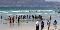 Law enforcement officers patrol Muizenberg beach as fishermen reel in a catch. (Photo: Victoria O’Regan)