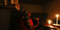 A South African woman carrying her daughter on her back runs her take away restaurant by candle light during a sheduled power outage known as load shedding in the impoverished neighbourhood of Masiphumelele, Cape Town, South Africa 26 May 2015. EPA/NIC BOTHMA