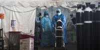 A nurses pushes an oxygen cylinder into an isolation tent for a patient. (Photo: Shiraaz Mohamed)