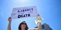 A woman holds an Anonymous mask and a placard stating "Give me LIBERTY OR GIVE ME DEATH" while joining demonstrators at a rally outside the Pennsylvania Capitol Building to protest the continued closure of businesses due to the coronavirus pandemic on May 15, 2020 in Harrisburg, Pennsylvania.  Pennsylvania Governor Tom Wolf has introduced a color tiered strategy to reopen the state with most areas not easing restrictions until June 4.  (Photo by Mark Makela/Getty Images)