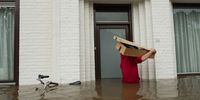 GEULLE, NETHERLANDS - JULY 16: A man carries a box through a flooded street on July 16, 2021 in Geulle, Netherlands. The flooding has been caused by unusually heavy rain in the hilly parts of Germany and the Ardennes region in Belgium. In Germany the death toll has now passed 100 with dozens more missing. Rescue and evacuation operations are now underway in tricky conditions across the affected regions. (Photo by Sanne Derks/ Getty Images)
