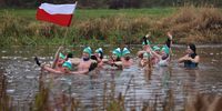 NAREWKA, POLAND - NOVEMBER 11: Revelers, one waving a Polish flag, celebrate Poland's National Day by taking a dip in the icy river that flows through their village near the Belarus border on November 11, 2021 in Narewka, Poland. Poland's National Day  marks the anniversary of the restoration of Poland's sovereignty from German rule in 1918. This year, Poland commemorates Naitonal Day under a state of emergency as the migrant crisis on the border with Belarus unfolds. (Photo by Sean Gallup/Getty Images)