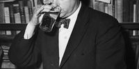 Welsh poet Dylan Thomas (1914 - 1953) drinking a glass of beer and smoking while seated at a desk with stacks of his books of poetry, New York City, c. 1950. (Photo by Hulton Archive/Getty Images)