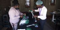Ponani Shikweni, left, and Paulos Romane, right, trim the strings of the masks to ensure they are of equal length. (Photo: Shiraaz Mohamed)