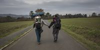 LIGONDE, SPAIN - NOVEMBER 24: Pilgrims Giulia Borsci, 33, from Italy (right) and Victor Bezerra, 25, from Brazil, hold hands during their four months journey on foot from Italy, following the Way of St. James, or El Camino de Santiago, a network of ancient pilgrim routes that stretch across Europe and converge at the tomb of St. James (Santiago in Spanish) in Santiago de Campostela in northwest Spain, on November 24, 2020 close to Ligonde, Galicia, Spain. The Camino de Santiago is being affected by Covid-19 with strict restrictions regarding services and mobility along the routes. Starting October 30, 2020, Spanish authorities closed among others, the  perimeter of Santiago de Compostela. Only pilgrims that have been journeying before October 30 can stop at the cathedral of Santiago de Campostela, but they are not allowed to stay overnight and have to transit through. (Photo by Siegfried Modola/Getty Images)