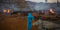 BENGALURU, INDIA - APRIL 30: A man wearing PPE (Personal Protective Equipment) watches mass cremations in a disused granite quarry repurposed to cremate the dead due to COVID-19 on April 30, 2021 in Bengaluru, India. With recorded cases crossing 380,000 a day and 3000 deaths in the last 24 hours, India has more than 2 million active cases of COVID-19, the second-highest number in the world after the U.S. A new wave of the pandemic has totally overwhelmed the country's healthcare services and has caused crematoriums to operate day and night as the number of victims continues to spiral out of control. (Photo by Abhishek Chinnappa/Getty Images)