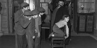 10th November 1959:  'Professor' Jimmy Edwards (1920 - 1988) in rehearsal at Shepherds Bush TV studios is administering a flogging to one of the pupils of 'Chiselbury' school, Paul Norman, watched by his classmates.  (Photo by Reg Speller/Fox Photos/Getty Images)