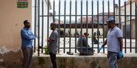 People wearing protective masks and gloves stand outside as men pray in a derelict yeard outside a mosque which has been closed in against the outbreak of Covid-19 Coronavirus, in Johannesburg, South Africa, 19 March 2020. Almost all places of worship have closed to members of the public as fears of the coronavirus epidemic mount. (Photo: EPA-EFE/YESHIEL PANCHA)