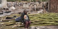 A young child sits on a pile of wood branches which residents are using to rebuild their homes. (Photo: Ihsaan Haffejee)</p>
<p>