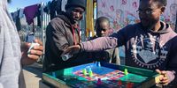 Men take turns in groups of four to play Ludo at the Bellville refugee camp. (Photo: Tariro Washinyira)