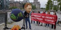 An activist dressed as German Finance Minister and leader of the German Free Democrats (FDP) Christian Lindner spins a globe over a mock fire as other activists hold a banner that reads: "The FDP is burning the future - stop the climate blockade!" near the Reichstag on May 23, 2023 in Berlin, Germany. The German government coalition of Social Democrats (SPD), Greens and FDP is in a internal conflict over a new proposed law to require that new home heating systems run on at least 65% renewable energy starting in 2024. The FDP is blocking the law, claiming its formulation is inadequate. (Photo by Sean Gallup/Getty Images)