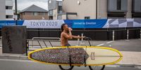 FUJISAWA, JAPAN - JUNE 28: A surfer cycles past a Tokyo Olympic banner on June 28, 2021 in Fujisawa, Japan. As the Olympic torch relay makes its way around Japan, much of the original route has been altered or cancelled completely as prefectural authorities act to avoid large gatherings while the country endures a fourth wave of coronavirus. (Photo by Yuichi Yamazaki/Getty Images)