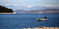 A fisherman steers his boat along the shoreline on February 5, 2010 in Corfu, Greece. Snow covered mountains in Albania can be seen in the distance.  (Photo by Dan Kitwood/Getty Images)