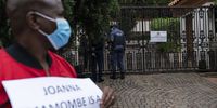A policeman talks to an official from the Zimbabwean Embassy while a man holds a placard saying political prisoner Joanah Mamombe is a GBV case because of conditions in Zimbabwean prisons. (Photo: Shiraaz Mohamed)