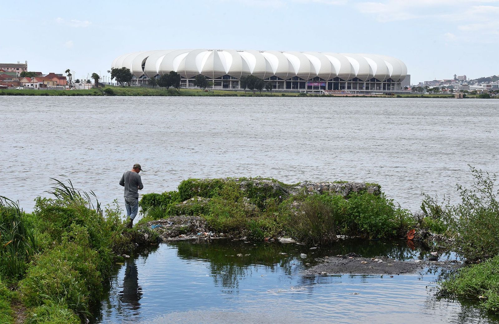 A man at a lake with a stadium in the background.