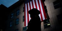 A first responder stands in front of a large American flag after it is unfurled on the side of the Pentagon to commemorate the 24th anniversary of the 9/11 terror attacks on September 11, 2025 in Arlington, Virginia. Later today, U.S. President Donald Trump will visit the Pentagon to lay a wreath to honor the victims of the September 11th terror attack. (Photo by Andrew Harnik/Getty Images)